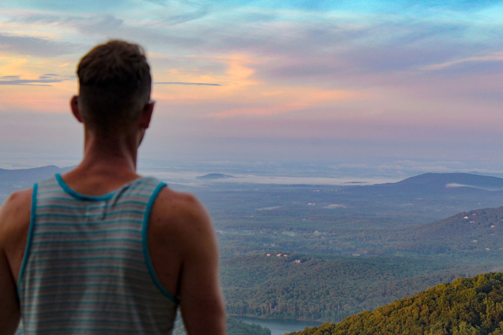 man in tank top looking at valley from mountaintop