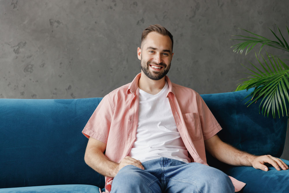 man in salmon shirt smiling on blue couch
