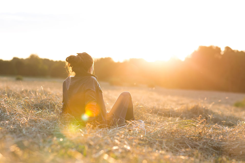 lady sitting in field looking at sunset