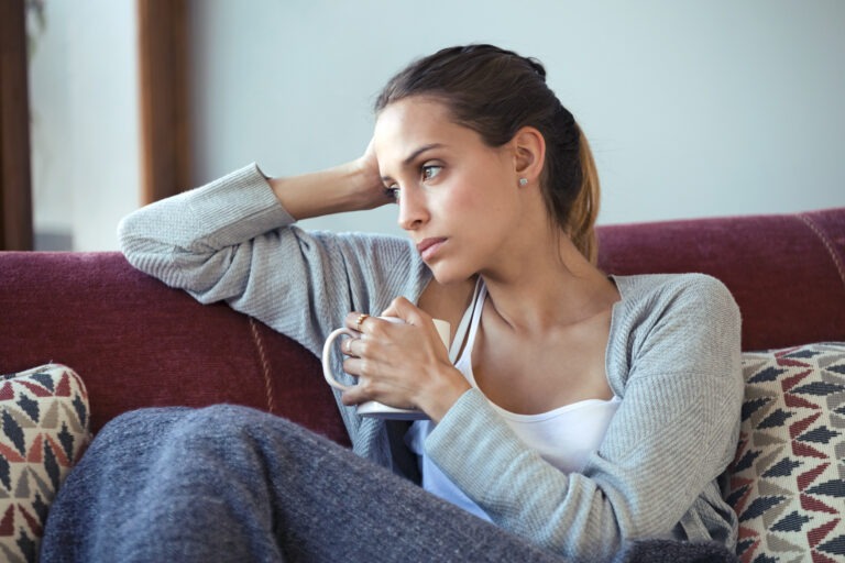 A woman sitting on a couch, appearing anxious and contemplative, symbolizing the emotional toll of delirium tremens during alcohol withdrawal.